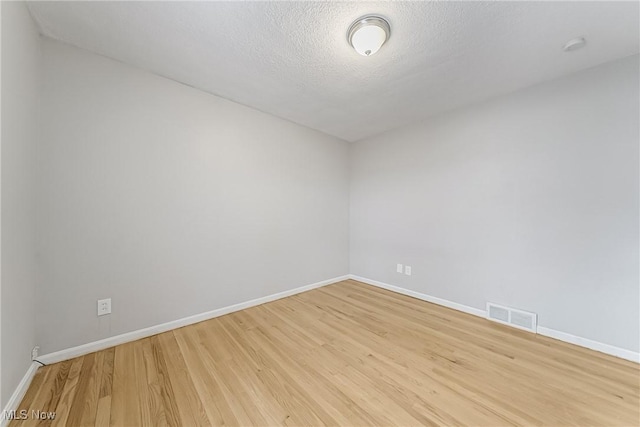 empty room with baseboards, visible vents, a textured ceiling, and light wood finished floors