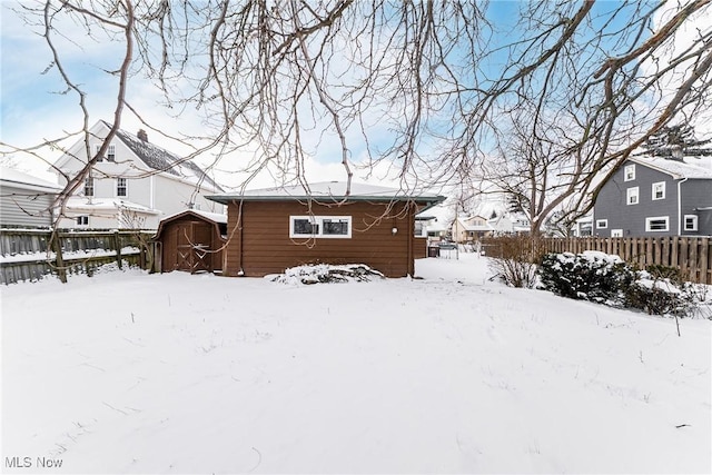 snow covered back of property featuring fence private yard, a storage shed, and an outbuilding