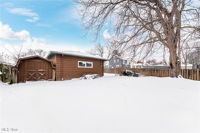 snow covered rear of property with a barn, fence, and an outbuilding