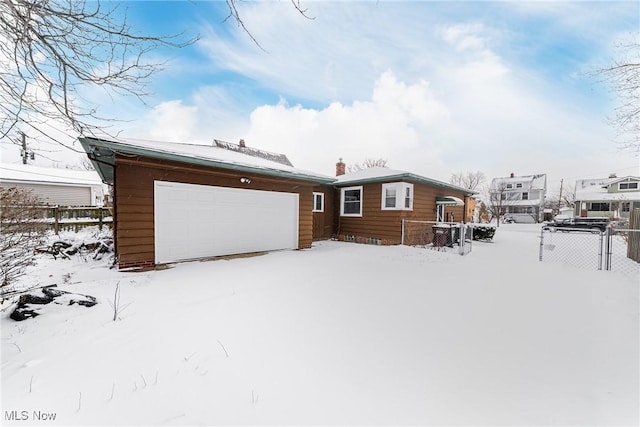 snow covered back of property featuring a garage, an outbuilding, and fence