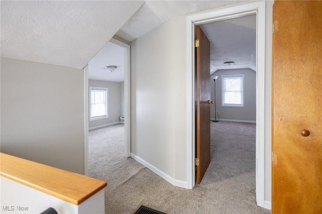 corridor with plenty of natural light, a textured ceiling, and light colored carpet