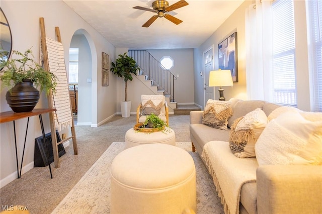 living area featuring light carpet, baseboards, arched walkways, ceiling fan, and stairway