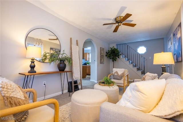 living room featuring arched walkways, a ceiling fan, baseboards, stairs, and carpet