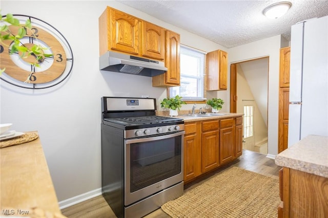 kitchen featuring under cabinet range hood, a sink, light countertops, stainless steel gas range, and light wood finished floors