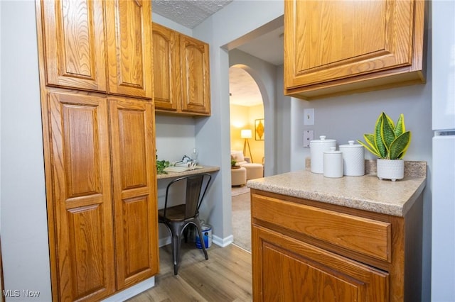 kitchen featuring arched walkways, light countertops, light wood finished floors, and brown cabinetry