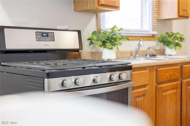 kitchen featuring brown cabinetry, stainless steel gas range oven, light countertops, and a sink