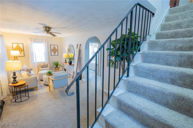 stairway with arched walkways, ceiling fan, carpet flooring, and baseboards