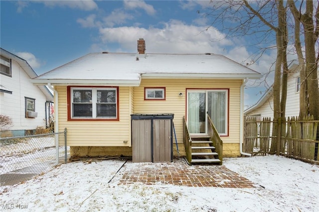 snow covered back of property featuring entry steps, a chimney, and fence