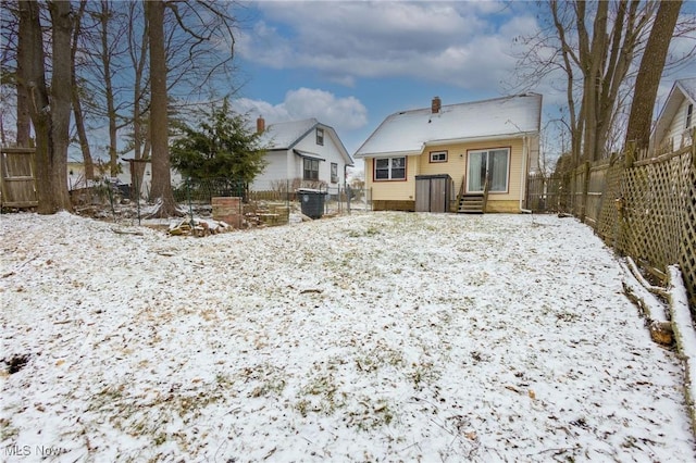 snow covered house featuring entry steps, a fenced backyard, and a chimney