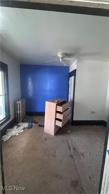 interior space featuring radiator heating unit, a ceiling fan, and baseboards