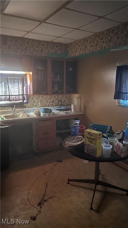 kitchen with a drop ceiling, glass insert cabinets, decorative backsplash, and a sink