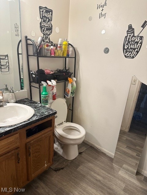 half bathroom with toilet, wood finished floors, vanity, and baseboards