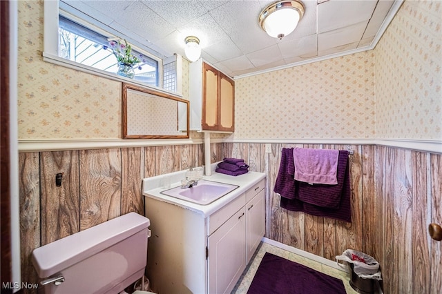 bathroom featuring toilet, wallpapered walls, a wainscoted wall, and vanity