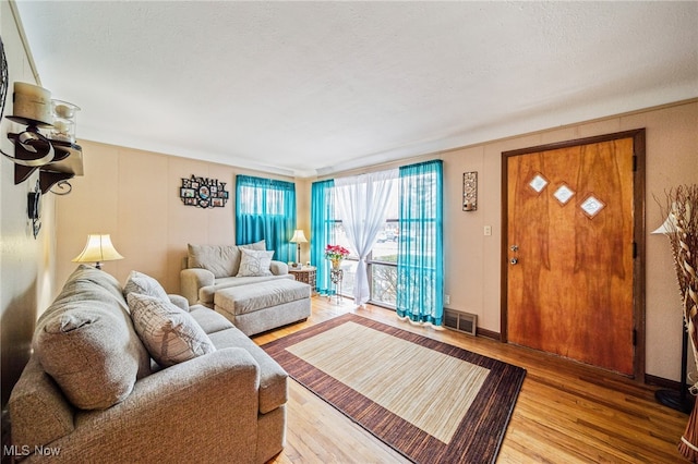 living room with light wood finished floors, baseboards, visible vents, and a textured ceiling