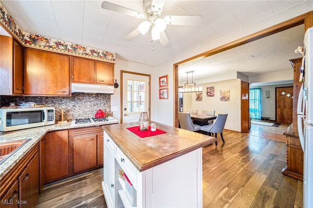 kitchen featuring white appliances, tasteful backsplash, wood-type flooring, brown cabinets, and under cabinet range hood