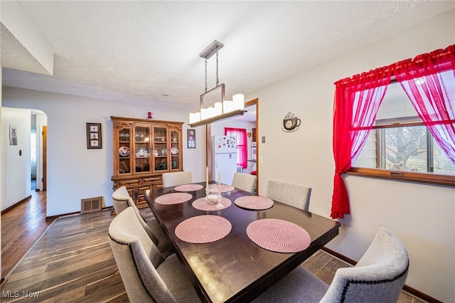 dining space featuring arched walkways, visible vents, a textured ceiling, wood finished floors, and baseboards