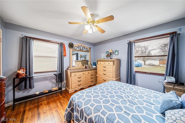 bedroom featuring ceiling fan, dark wood-style flooring, multiple windows, and baseboards