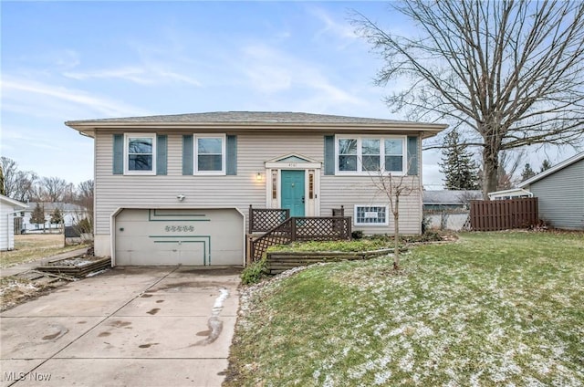 raised ranch featuring concrete driveway, an attached garage, fence, and a front yard