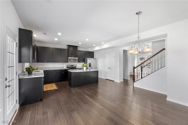 kitchen with dark cabinets, stainless steel appliances, dark wood-style flooring, light countertops, and a center island