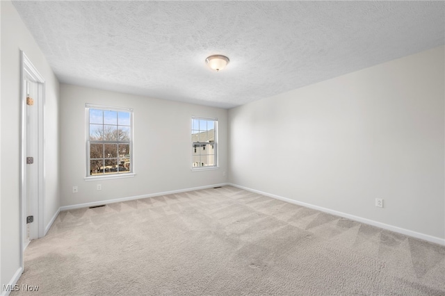 empty room featuring light carpet, a textured ceiling, and baseboards