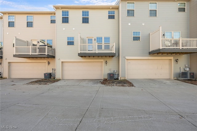 back of house featuring driveway, an attached garage, and central AC