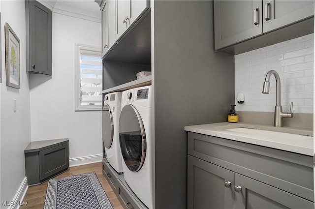 clothes washing area with a sink, wood finished floors, baseboards, cabinet space, and washing machine and clothes dryer