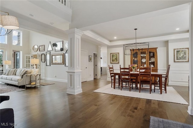 dining space featuring a raised ceiling, a decorative wall, dark wood finished floors, and ornate columns