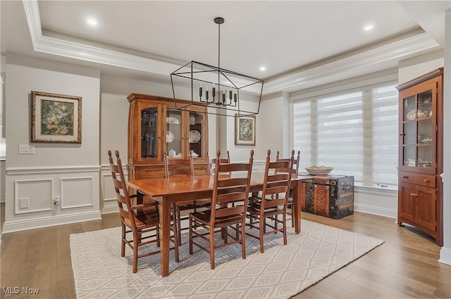 dining area featuring crown molding, a raised ceiling, a decorative wall, an inviting chandelier, and wood finished floors