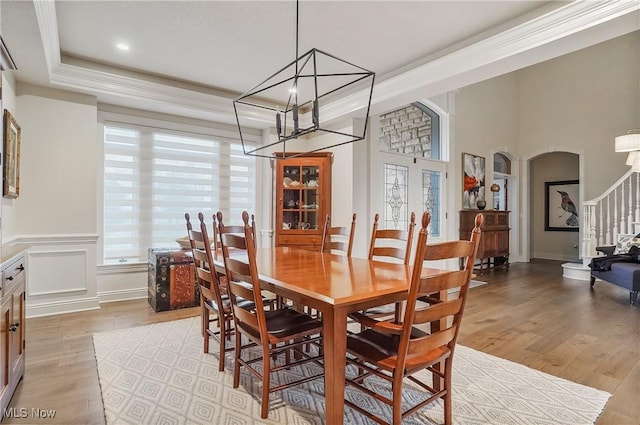 dining area featuring arched walkways, light wood-type flooring, a raised ceiling, and stairs