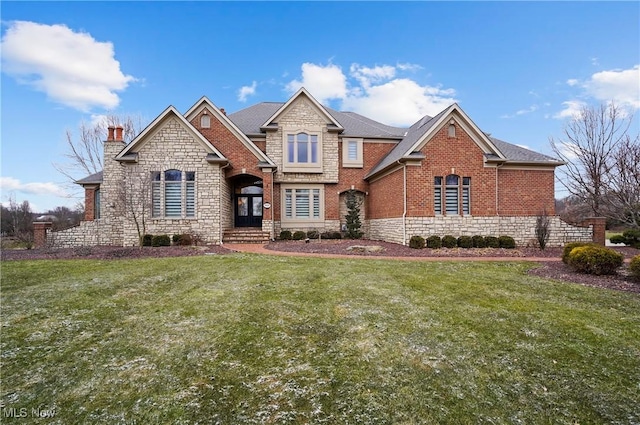 view of front of property featuring a front yard, stone siding, brick siding, and a chimney