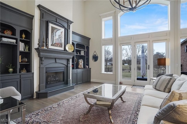 living area with baseboards, a fireplace with raised hearth, wood finished floors, a high ceiling, and a notable chandelier