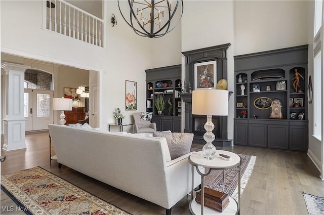 living area with french doors, a towering ceiling, an inviting chandelier, wood finished floors, and ornate columns