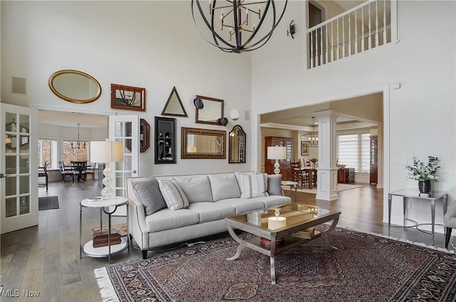 living room with wood finished floors, plenty of natural light, ornate columns, and an inviting chandelier