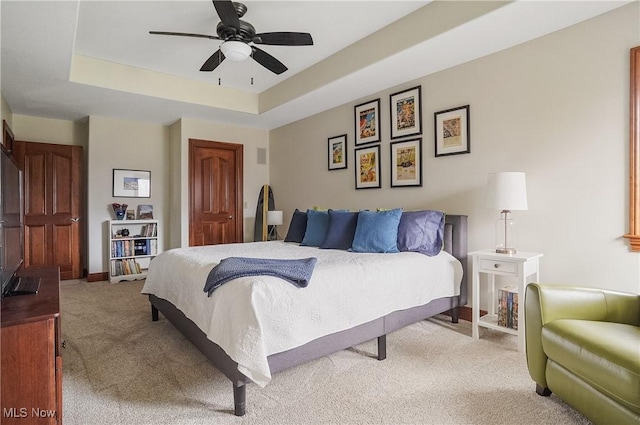 bedroom featuring a closet, a raised ceiling, light carpet, ceiling fan, and baseboards