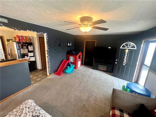 playroom with carpet flooring, a fireplace, a textured ceiling, and ceiling fan