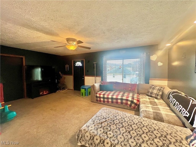 living area featuring ceiling fan, a lit fireplace, a textured ceiling, and carpet