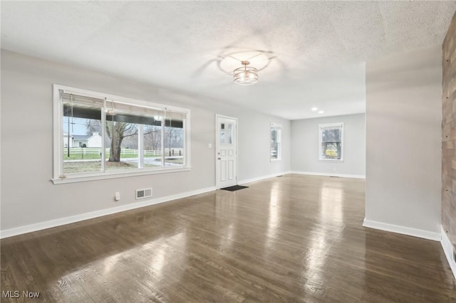 unfurnished living room with visible vents, a textured ceiling, baseboards, and wood finished floors