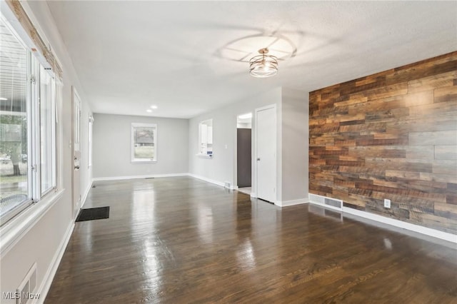 unfurnished living room featuring wooden walls, baseboards, visible vents, an accent wall, and wood finished floors