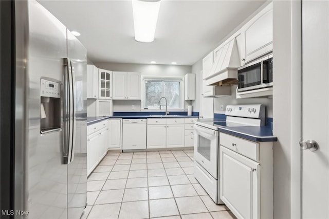 kitchen with dark countertops, appliances with stainless steel finishes, premium range hood, white cabinetry, and a sink