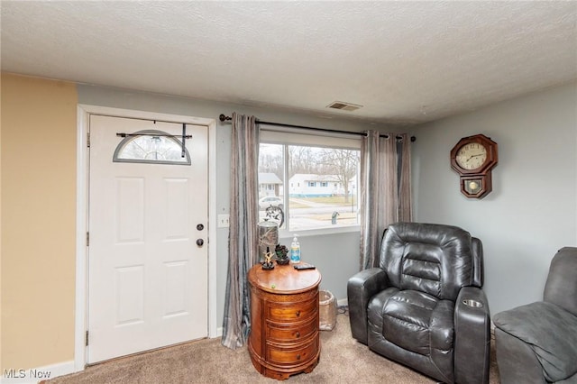 entryway with baseboards, visible vents, a textured ceiling, and light colored carpet