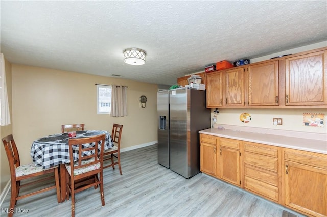 kitchen with light wood-style flooring, light countertops, stainless steel refrigerator with ice dispenser, and a textured ceiling