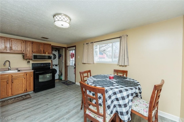 kitchen with stacked washer and dryer, light wood-style flooring, stainless steel microwave, black electric range oven, and a sink