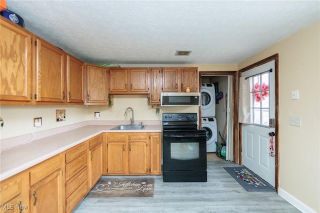 kitchen with stacked washer and dryer, black electric range oven, stainless steel microwave, visible vents, and a sink