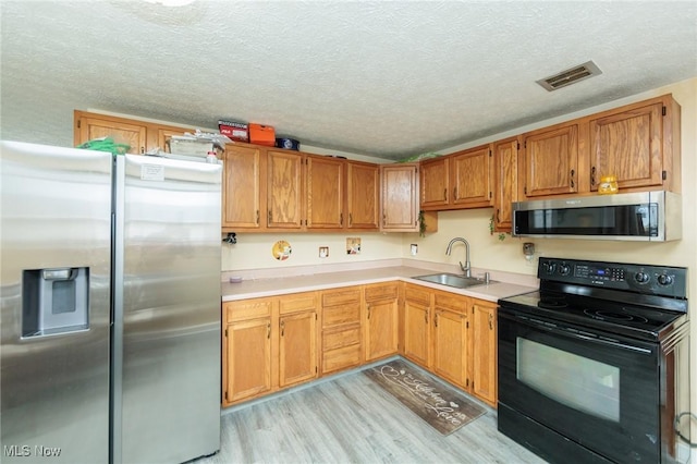 kitchen featuring stainless steel appliances, a sink, visible vents, light countertops, and light wood-type flooring