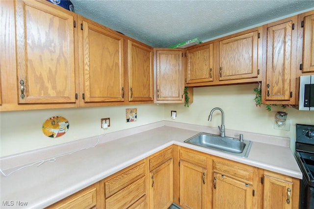 kitchen with light countertops, stainless steel microwave, a sink, a textured ceiling, and range