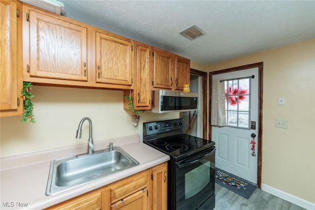 kitchen featuring stainless steel microwave, light countertops, a textured ceiling, black electric range, and a sink