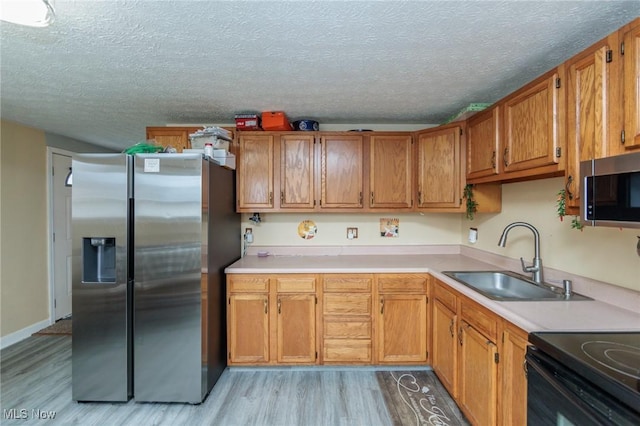 kitchen with light countertops, appliances with stainless steel finishes, a sink, a textured ceiling, and light wood-type flooring