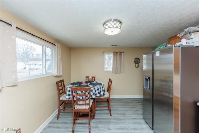 dining space with plenty of natural light, baseboards, light wood-style flooring, and a textured ceiling