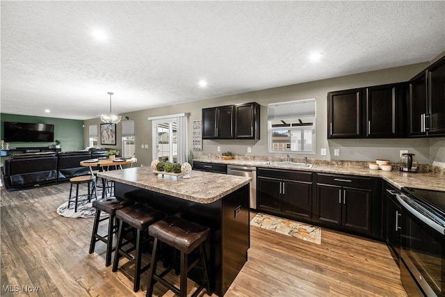 kitchen with a center island, a kitchen breakfast bar, appliances with stainless steel finishes, light wood-style floors, and a sink