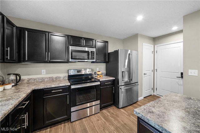 kitchen with light countertops, light wood finished floors, dark cabinets, and appliances with stainless steel finishes